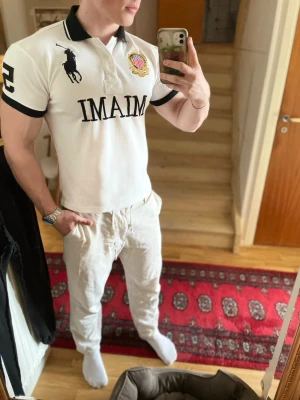 Vit Ralph Lauren Miami piké  - Vit piké från Ralph Lauren med svart tryck 'MIAMI' på bröstet, stor logga och emblem. Svarta detaljer på krage och ärmslut samt stor svart siffra 5 på ryggen. Klassisk pikékrage och korta ärmar. Perfekt för en sportig och stilren look.