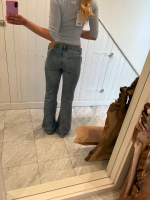 Ljusblå bootcut jeans med låg midja - Säljer ett par ljusblå bootcut jeans med låg midja och klassiska femficksdetaljer. Jeansen har en avslappnad passform och är tillverkade i denim. Perfekta för en trendig och avslappnad stil.