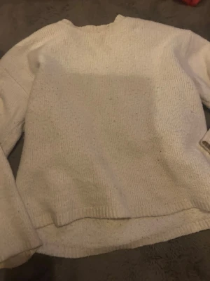 Beige stickad tröja med rund hals - Mysig beige stickad tröja med rund hals och långa ärmar. Tröjan har en enkel, rak passform och ribbstickade muddar vid ärmslut och nederkant. Perfekt för lager på lager under kyliga dagar.