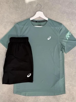 Träningsset från Asics i grönt och svart - Snyggt träningsset från Asics med en ljusgrön t-shirt och svarta shorts. T-shirten har rund hals, kort ärm och Asics-logga på bröstet och ärmen. Shortsen har elastisk midja och logga på benet. Perfekt för gym eller löpning.