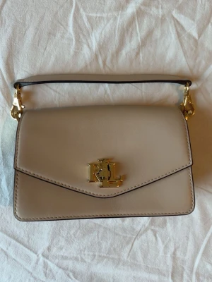 Beige handväska Ralph Lauren - Liten handväska i slätt läder från Ralph Lauren. Avtagbart axelband! (Själva märket på framsidan har repor! Om fler bilder behövs skriv.)🤍priset går att diskutera!