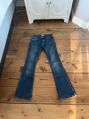 Blå bootcut jeans med slitningar - Säljer ett par blå bootcut jeans med lätt slitna detaljer och klassisk femficksdesign. Jeansen har normal midja och utsvängda ben, perfekta för en avslappnad och trendig look. Materialet är denim i bomull med en snygg tvättad finish.