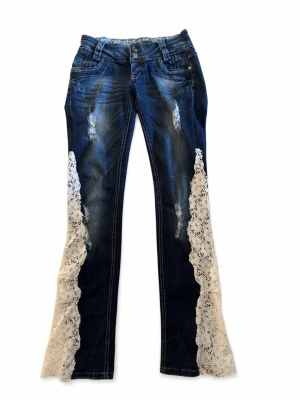 Blå bootcut jeans med spetsdetaljer - Unika blå bootcut jeans med slitningar och vita spetsdetaljer längs benen. Jeansen har låg midja