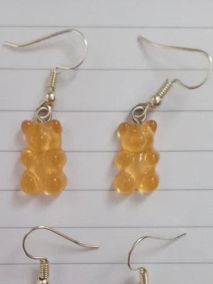 Gula björn örhängen - Säljer ett par unika örhängen med gula gummibjörns-hängen i plast. Örhängena har krokar i metall och är knappt använda. 