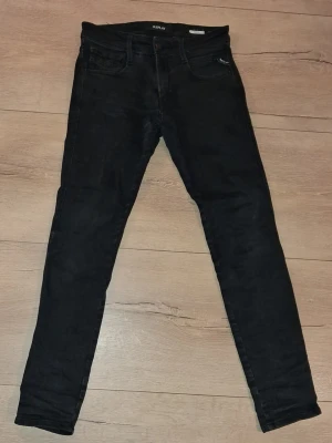 Svart Replay jeans - Säljer ett par svarta jeans från Replay anbass med klassisk femficksdesign.. Jeansen har smal passform och är tillverkade i stretchigt denimtyg för extra komfort. Perfekta för en trendig och avslappnad look. 