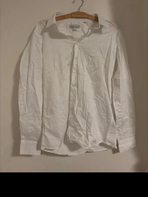 Vit klassisk skjorta i bomull - En stilren vit herrskjorta från med klassisk krage och knappar framtill. Skjortan är långärmad och i slim fit. Ny utan prislapp