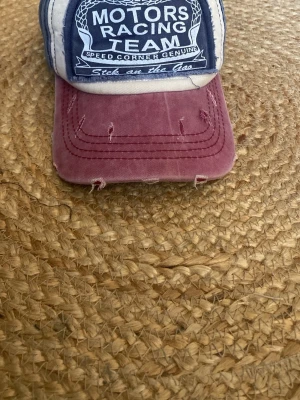 Motors Racing Team keps blå/vinröd - Snygg keps med blått och vitt tyg samt vinröd skärm. Den har slitningar som man kan se och den ska vara så! Man kan ändra storleken.