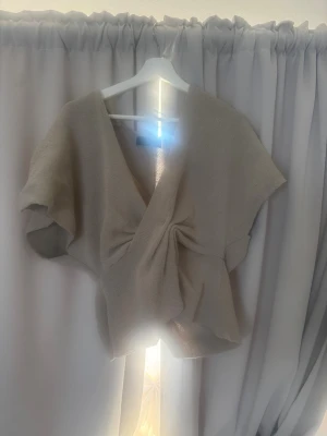 Beige omlottopp från Zara - Säljer en ljusgrön omlottopp från Zara med korta ärmar och v-ringad design. Toppen är stickad och har en snygg drapering framtill som ger en cool och modern look. Perfekt för dig som gillar stilrena och trendiga plagg. Perfekt till sommaren. Använd en gång 