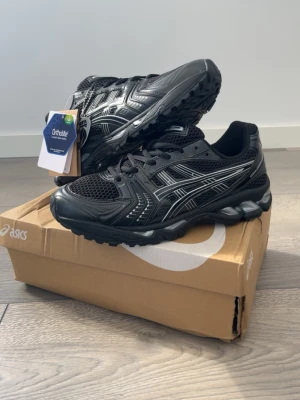 Svarta Asics Gel sneakers - Snygga svarta Asics Gel sneakers med Ortholite innersula. Skorna har mesh och syntetmaterial i ovandelen, silverfärgade detaljer och en robust sula som ger bra komfort. Perfekta för dig som gillar sportig stil och vill ha något som sticker ut.