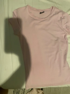 Ljusrosa t-shirt från Gina Tricot - En basic ljusrosa t-shirt från Gina Tricot i mjuk bomull. Modellen är klassisk med rund halsringning och korta ärmar. Perfekt att matcha med jeans eller kjol för en enkel och fräsch look.
