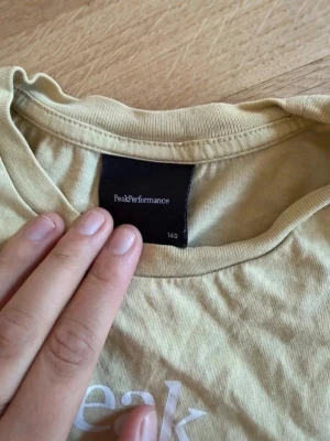 Beige Peak Performance t-shirt - Snygg vit t-shirt från Peak Performance med vit logga och texten 'Est. 1986' på bröstet. Klassisk rund halsringning och korta ärmar. Perfekt till jeans eller shorts för en avslappnad stil.