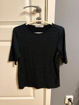 Svart glittrig topp från Pieces - Snygg svart topp från Pieces med grönt/blått glittrigt material och rund halsringning. Storlek XS, använd 1 gång. 