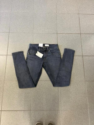 Grå slim fit jeans från tiger of sweden - Snygga blå slim fit jeans från tiger of sweden med klassisk femficksdesign och dragkedjegylf. Jeansen har en diskret tvättad look och är tillverkade i ett mjukt denimtyg som sitter skönt. Perfekta för en avslappnad och trendig stil.