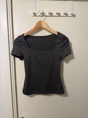 Mörkgrå topp med fyrkantig hals - En stilren mörkgrå topp med fyrkantig halsringning och korta ärmar. Perfekt för att matcha med jeans eller kjol. Materialet känns mjukt och stretchigt, vilket gör den bekväm att bära hela dagen.