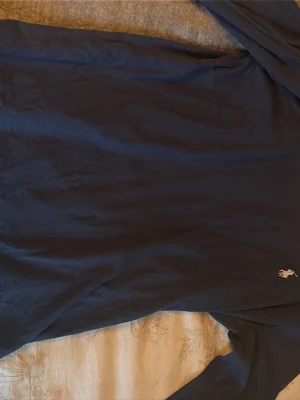 Blå långärmad topp från Polo Ralph Lauren - Mörkblå långärmad topp från Polo Ralph Lauren med klassisk passform. Tillverkad i mjuk bomull och har den ikoniska lilla broderade loggan på bröstet. Perfekt till jeans eller kjol för en clean och stilren look.