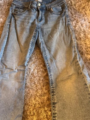 Ljusblå bootcut jeans - Säljer ett par ljusblå jeans med boot cut passform och klassisk femficksdesign. Jeansen har normal midja och stängs med knapp och dragkedja. Perfekta för en avslappnad och trendig look.