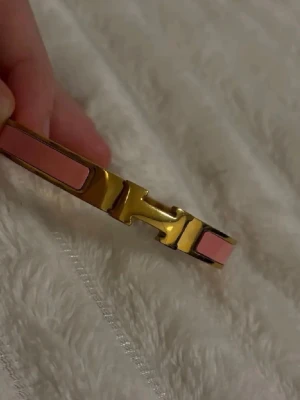 Guldigt armband med rosa detaljer - Säljer ett ikoniskt Clic H armband i guldfärgad metall med ljusrosa emaljdetaljer. Armbandet har en stilren och elegant design med det klassiska H-spännet framtill. Helt ny! Minsta storleken.🧡