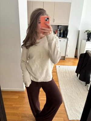 Beige stickad tröja med rund hals - En enkel och snygg beige stickad tröja med rund hals och ribbade muddar. Tröjan har en avslappnad passform och långa ärmar, perfekt att matcha med jeans eller mjukisbyxor. Materialet ser ut att vara mjukt och bekvämt, idealiskt för kyliga dagar.