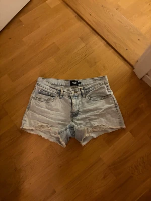 Ljusblå jeansshorts från 157 - Snygga ljusblå jeansshorts från 157 med fransiga kanter och slitna detaljer. Klassisk femficksmodell och hög midja. Perfekta för varma dagar och enkel att matcha med allt.