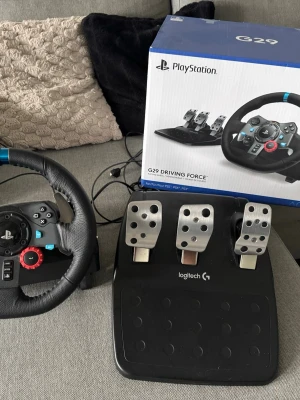 Logitech G29 ratt och pedaler - Säljer en Logitech G29 Driving Force ratt och pedalset för PlayStation. Ratten har svart läderklädsel, blå detalj upptill och flera knappar inklusive PlayStation-knappar. Pedalerna är i metall och svart plast. Perfekt för racing och simracing.