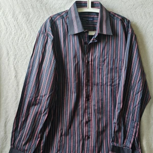 Randig skjorta från Tommy Hilfiger - Snygg skjorta från Tommy Hilfiger med ränder i svart, rött, blått och vitt. Klassisk krage, bröstficka och långa ärmar. Perfekt för dig som gillar stilrena detaljer och vill sticka ut lite extra.