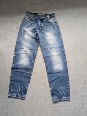 Blå distressed jeans från Donna Jeans - Säljer ett par blå jeans från Donna Jeans med slitna detaljer och ljusa tvättade partier. Jeansen har raka ben, klassisk femficksmodell och synliga slitningar för en trendig look. Perfekta för dig som gillar streetstyle och avslappnad stil.