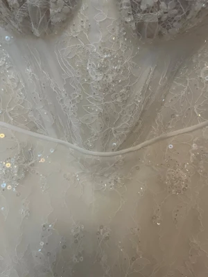 Vit spetsklänning med paljetter - Romantisk vit klänning med vacker spets och glittrande paljetter. Klänningen har markerad byst, axelbandslös design och fina broderade detaljer. Perfekt för dig som vill sticka ut med en elegant och feminin look.