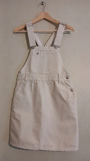 VINTAGE 90-TAL: Naj-Oleari hängselklänning - Naj-Oleari är ett ikoniskt italienskt märke som grundades 1916 och nådde kultstatus under 80- och 90-talet. Märket blev synonymt med den italienska ungdomskulturen ("Paninari") och var en stor statussymbol tack vare sin höga kvalitet och sina unika detaljer. Denna hängselklänning i 100% bomull är en del av italiensk modehistoria. Idag är Naj-Oleari främst verksamma inom skönhetsbranschen, vilket gör deras originalplagg från storhetstiden till eftertraktade samlarobjekt. 