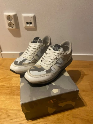 Valentino rockrunners - Snygga Valentino rockrunners med vitt och grått camo-mönster. Skorna har svarta sulor med valentinos klassiska spetsar baktill. Skorna är i storlek 42. De är använda men i bra skick, passar perfekt till det mesta! Original box med valentino tygpåse medföljer också. 