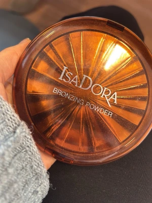 IsaDora Bronzing Powder bronzer - IsaDora Bronzing Powder i en stor rund dosa med bronsfärgat lock. Pudret har en varm, ljusbrun ton och ger en naturlig solkysst look. Hyfsat bra skick 