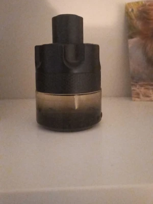 Svart parfymflaska från Azzaro - Säljer en parfym från Azzaro i en stilren svart och transparent flaska med rund form. Flaskan har en robust design med texturerad yta upptill och slät glasdel nedtill. Perfekt för dig som gillar eleganta och moderna dofter.