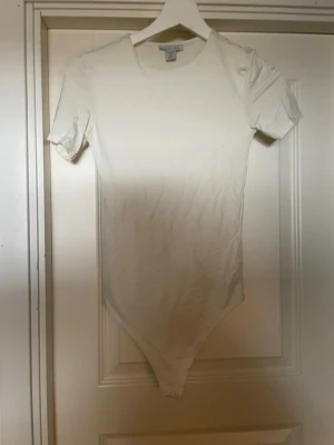 Vit kortärmad body  - En stilren vit body med korta ärmar och rund halsringning. Tillverkad i mjukt stretchigt material som sitter tajt mot kroppen. Perfekt att styla med jeans eller kjol för en clean look. Använd enstaka gågn