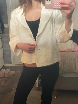 Trekvartsärmad jacka - Snygg vit kavaj med bred krage och trekvartsärmar. Jackan har dekorativa strukturdetaljer vid ärmslut och nederkant samt knäppning framtill. Perfekt för dig som vill ha en stilren och trendig look. Vet ej vilken storlek men passar xs-m