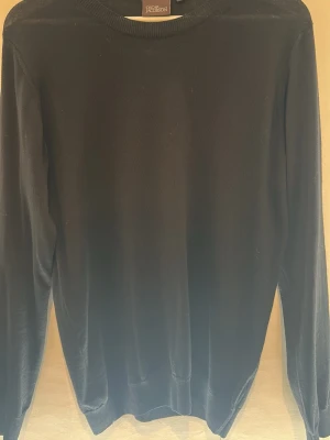 Oscar Jacobson tröja - Klassisk svart stickad tröja från Oscar Jacobson med rund halsringning och ribbade muddar. Tillverkad i Italien och har en stilren, enkel design som passar till det mesta. Perfekt basplagg för garderoben. Super liten fläck är 100% säker den går bort i tvätten 