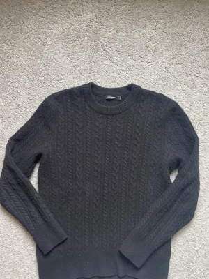 Mörkblå kabelstickad tröja från J. Lindeberg - Riktigt snygg kabelstickad tröja i 100% kvalitativ ull från J. Lindeberg. Den är använd men har inga vidare tecken på användning eller skador alls. Är mindre i storleken då jag anser att den snarare är i storlek Small än Medium som det står att den är på lappen. Perfekt för någon mellan 167-174