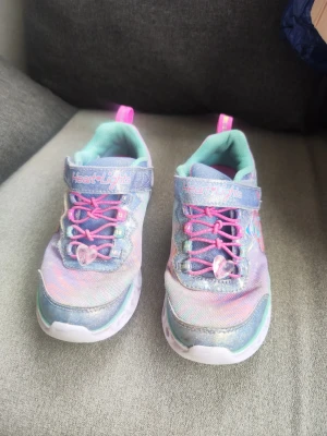 Skechers Heart Lights pastell sneakers  - Färgglada Skechers Heart Lights sneakers i pastellfärger med glittereffekt. Skorna har rosa elastiska skosnören, kardborreband och hjärtformade detaljer i sulan. Storleken är EU 30. Det är barnskor. Skorna ljuser inte upp länge, ljuset fungerar inte. 