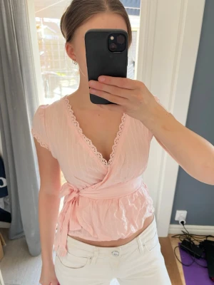 Ljusrosa omlottblus  - Supersöt ljusrosa omlottblus med knyt i midjan och fina spetsdetaljer längs v-ringningen. 