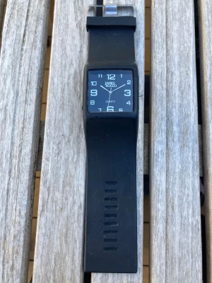James Rocco Quartz 40mm  - Svart James Rocco Quartz armbandsur med en rektangulär urtavla och vita arabiska siffror. Klockan har ett svart silikonarmband och ett silverfärgat spänne. Urverket är kvarts. Gott skick enligt bilder. Behöver batteri.  Nypris: 500 SEK Mitt pris: 189 SEK  Skickas alltid snabbt och spårbart. Skriv vid frågor och se gärna mina andra annonser!
