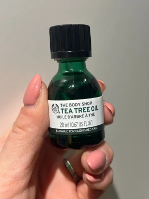 Tea Tree Oil från The Body Shop 20ml - Tea Tree Oil från The Body Shop i en grön glasflaska med svart skruvkork. Innehåller 20 ml olja, perfekt för oren hud. Enkel att använda och smidig att ta med sig. Märket är känt för sina naturliga ingredienser och fräscha doft.