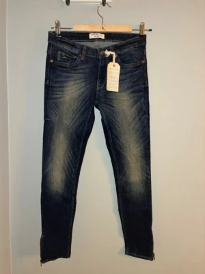 Mörkblå skinny jeans med dragkedja 27/32 - Snygga mörkblå skinny jeans med slitningar och dragkedjor vid bensluten. Klassisk femficksmodell och låg midja. Perfekta till sneakers eller boots. Jeansen har en cool tvätt och detaljer som ger en trendig look.