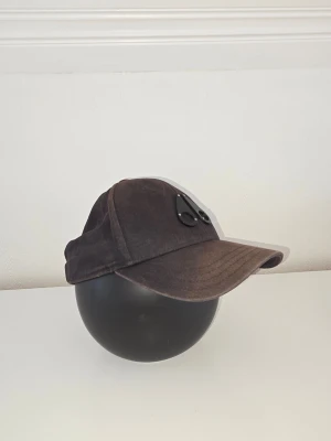 Svart keps från Moose Knuckles - Cool svart keps med unika glasögon-liknande detaljer framtill. Kepsen har böjd skärm och är tillverkad i ett slitstarkt tygmaterial. Perfekt för dig som vill sticka ut med en accessoar som har streetkänsla och edge.