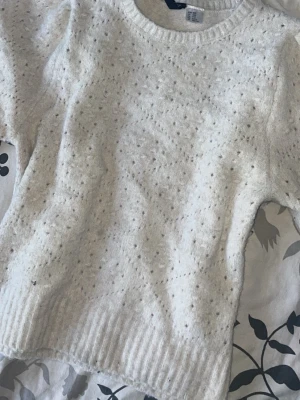 Vit stickad tröja med struktur - Mysig vit stickad tröja med prickig struktur och rund hals. Tröjan har ribbade muddar vid ärmslut och nederkant, samt en avslappnad passform. Perfekt för kyliga dagar och enkel att matcha med olika outfits.