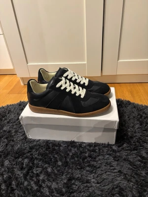 Svarta sneakers med vit sula - Stilrena svarta sneakers med vita skosnören och brun gummisula. Ovandelen är i en mix av mocka och läder, vilket ger en snygg kontrast och premiumkänsla. Klassisk låg modell som passar till det mesta. Perfekta för dig som gillar minimalistisk och tidlös stil.