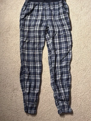Rutiga blå pyjamasbyxor - Mysiga pyjamasbyxor i blått och vitt rutigt mönster och fickor. Byxorna har resår i midjan och vid bensluten samt sidofickor. Perfekta för chillkvällar hemma. Materialet är mycket mjukt och skönt! Använda men finns inga slitningar! Är storlek 158/164 men skulle säga att det passar xs också.