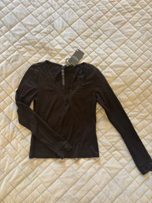 Svart långärmad topp med spets - Snygg svart långärmad topp från lager 157 med v-ringning och spetsdetaljer vid halsringningen och ärmsluten. Toppen är oanvänd🌸