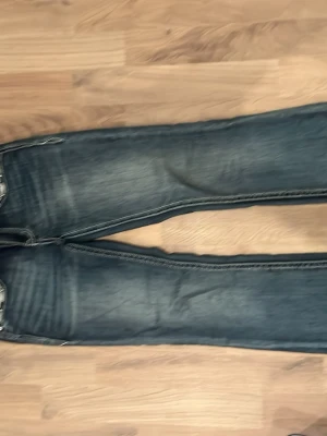 Mörkblåa Miss Me jeans med brodyr - Säljer ett par mörkblåa jeans från grace in LA med snygga  och detaljerade broderier på bakfickorna vilket är kors. Jeansen är flared. Nyköpa och knappt använda storlek 25 i jeans, köpta i London köpte för 2000