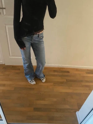 Blå bootcut jeans med fin design på fickorna - Säljer ett par ljusblå bootcut jeans med snygg  detalj på bakfickan. Jeansen har låg midja och klassisk femficksdesign. Perfekta för dig som gillar en avslappnad och trendig stil.