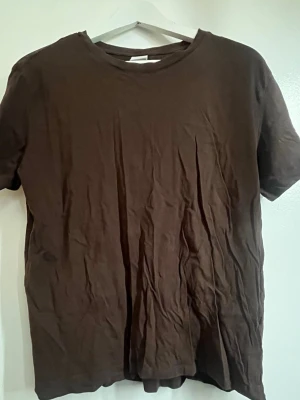 Brun basic t-shirt i bomull - En enkel brun t-shirt med rund hals och korta ärmar. Tillverkad i mjuk bomull och har en klassisk passform som funkar till det mesta. Perfekt att matcha med jeans eller shorts för en clean look.