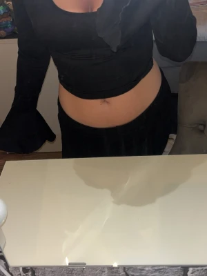 Svart croppad topp med volangärm - Snygg svart croppad topp från Shein med långa ärmar och breda volangdetaljer vid ärmsluten. Toppen har en rund halsringning och är tillverkad i ett stretchigt material som sitter bekvämt på kroppen. Perfekt för att skapa en trendig look. 
