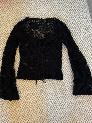 Svart spetsblus med snörning - Supersnygg svart blus i spets från Pieces med långa ärmar och snörning framtill. Blusen har en figurnära passform och v-ringad hals. använt några gånger🥰